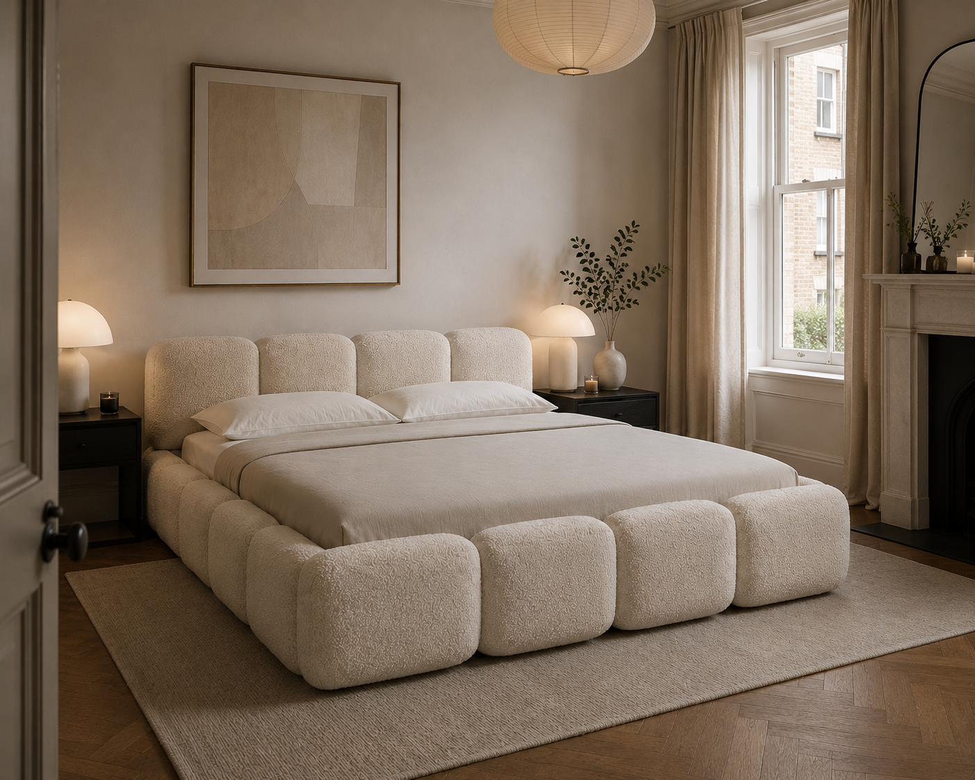 A modern low-profile bed with a chunky, tufted boucle upholstered frame in a warm cream color, styled in a cozy, minimalist bedroom with matching beige curtains, bedside tables, and a large abstract painting on the wall.