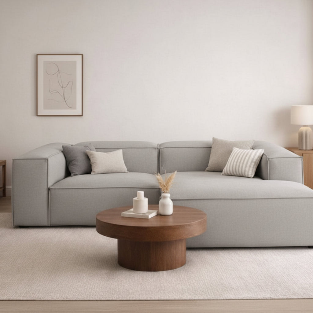 Alpha 2 seater sofa with chaise end in neutral fabric, styled in a modern living room with a round coffee table