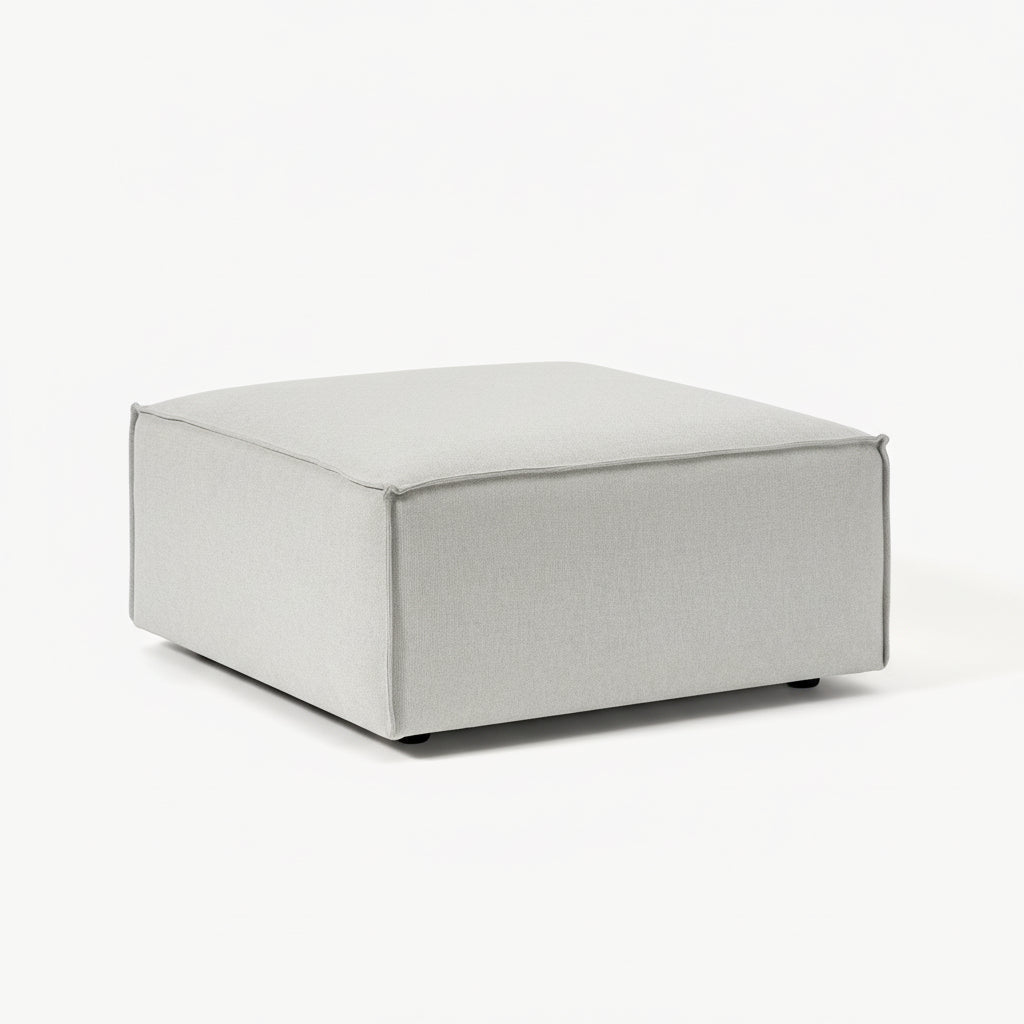 A clean, structured ottoman with a minimalist form, designed to complement modular seating with added versatility and comfort.