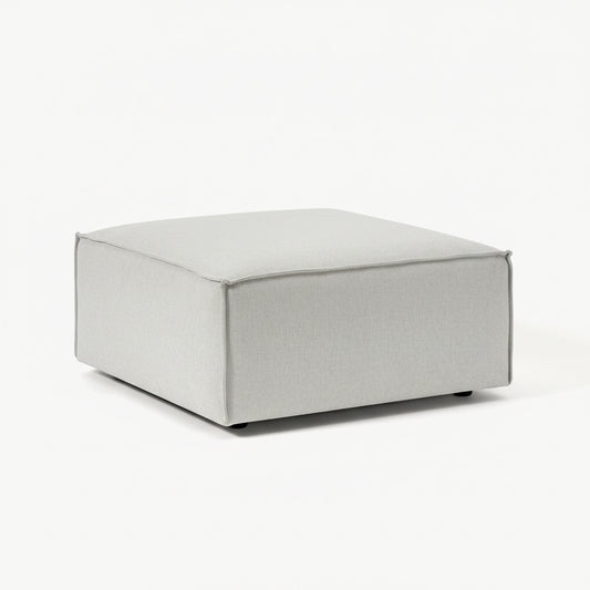 A clean, structured ottoman with a minimalist form, designed to complement modular seating with added versatility and comfort.