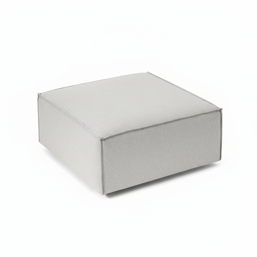 A clean, structured footstool with a low-profile silhouette, designed to complement modular seating while offering versatile comfort and functionality.
