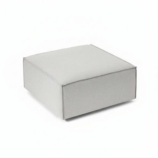 A clean, structured footstool with a low-profile silhouette, designed to complement modular seating while offering versatile comfort and functionality.