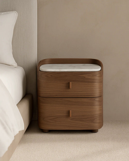 The Weston Bedside Table is displayed in a clean studio setting on a white background, showcasing its curved walnut veneer body and elegant Bianco Carrara marble top.